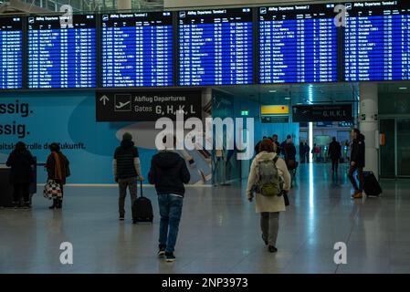 München, Deutschland - Februar 20,2023: Passagiere gehen unter einer Abflugtafel und einem Schild in deutschland, das die Abflugsteige am Flughafen Munioch anzeigt. Stockfoto