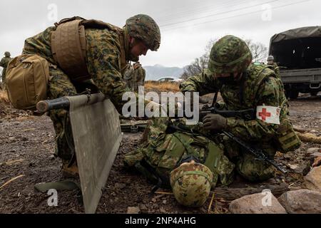 Hijudai, Japan. 19. Februar 2023. USA Marinekorpse mit der 31. Marineexpeditionstruppe und ein Soldat mit dem 1. Amphibien-Schnelleinsatzregiment, Japan Ground Self-Defense Force, bereiten sich darauf vor, ein simuliertes Opfer auf eine Trage zu heben, während einer Massenübung mit Verletzten in Hijudai, Japan, am Februar. 19, 2023. Das Training simulierte ein Massenunfallereignis, das dem beidseitigen medizinischen Team die Möglichkeit gab, während der Iron Fist 23 unter genau simulierten Druck und Bedingungen aktiv medizinische Versorgung vor Ort zu praktizieren. Iron Fist ist eine jährliche bilaterale Übung zur Steigerung der Int Stockfoto