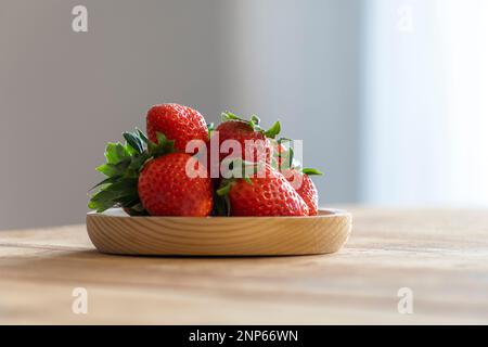 Ein Set Erdbeeren auf einem Holzteller auf dem Tisch in einer gut beleuchteten Küche Stockfoto