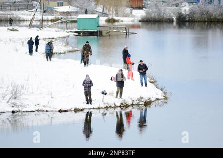 Die Menschen sind Fischer an beiden schneebedeckten Ufern des Sees bei der Konkurrenz in Russland im Wald Stockfoto