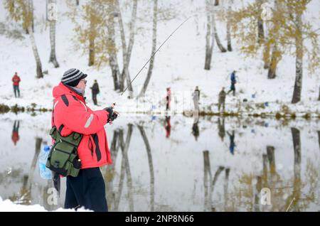 Die Menschen sind Fischer an beiden schneebedeckten Ufern des Sees bei der Konkurrenz in Russland im Wald Stockfoto