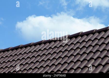 Modernes dunkelbraunes, bogenförmiges, toniges, geneigtes Wohndach. Blauer Himmel und weiße Wolken. Baukonzept. Modernes Dachwerkstoffkonzept. Stockfoto