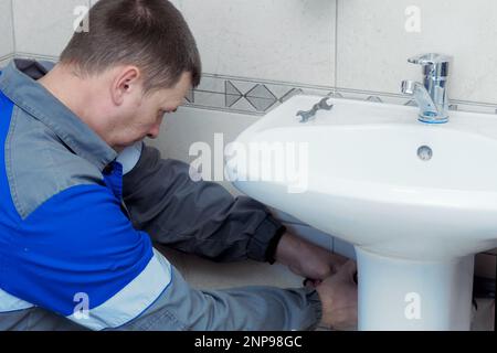 Professioneller Klempner in der Arbeitskleidung repariert Waschbecken in der Toilette. Aufrichtiger Arbeiter. Stockfoto