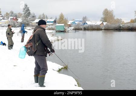 Die Menschen sind Fischer an beiden schneebedeckten Ufern des Sees bei der Konkurrenz in Russland im Wald Stockfoto