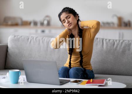 Müde Inderin, Die Nackenschmerzen Erleidet, Während Sie Mit Einem Notebook Zu Hause Arbeitet Stockfoto