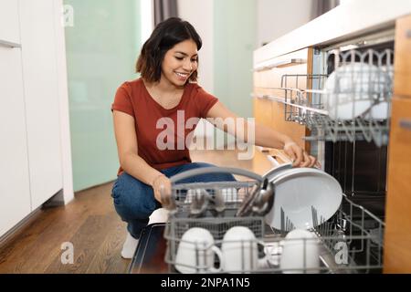 Wunderschöne Junge Araberin, Die Schmutzige Teller In Die Spülmaschine In Der Küche Lädt Stockfoto