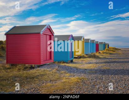 Ein Blick entlang der wunderschönen, lebendigen Strandhütten am Findhorn unter herrlichem blauen Himmel. Stockfoto