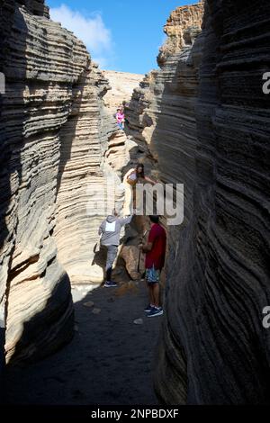 Touristen, die in Schichten von Ladera del volcan Las Grietas Lanzarote, Kanarische Inseln, Spanische vulkanische Felsformationen durch Erosion spazieren gehen Stockfoto