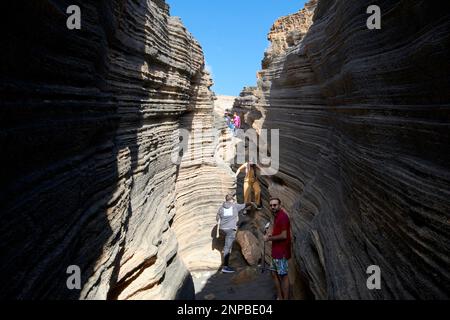 Touristen, die in Schichten von Ladera del volcan Las Grietas Lanzarote, Kanarische Inseln, Spanische vulkanische Felsformationen durch Erosion spazieren gehen Stockfoto