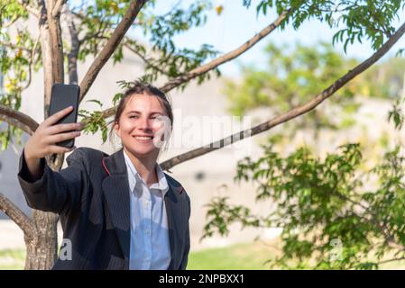 Lächelnde Geschäftsfrau, die im Freien mit einem Mobiltelefon Selfies macht. Stockfoto