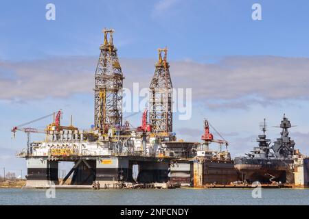 Galveston, Texas, USA - Februar 2023: Ölbohranlagen im Hafen der Stadt für Wartung und Reparatur, in denen das historische Kriegsschiff USS Texas restauriert wird Stockfoto