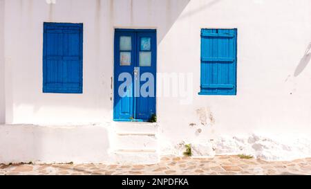 Ein Blick aus der Nähe auf ein weiß getünchtes Gebäude mit blauen Türen und Fenstern im Plaka in Milos. Stockfoto