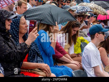 Um den Regenschirm näher zu halten und vor Regen zu schützen, gibt eine Dame der Kamera versehentlich den Finger beim Queen's Club Tennis Turnier. Stockfoto