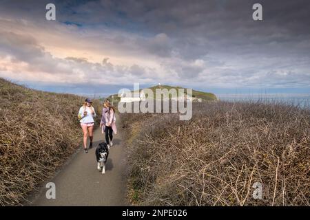 Hundespaziergänger und ein Hund genießen einen Spaziergang auf dem Küstenpfad rund um Newquay in Cornwall in Großbritannien. Stockfoto