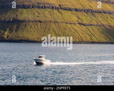 Klaksvík, Färöer - September 2020: Blick vom Hafen in Syðradalur auf der Insel Kalsoy auf die Gipfel der Insel Kunoy und das Fischermoto Boot während des Fischens Stockfoto