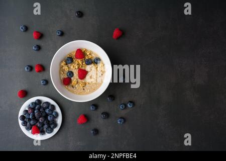 Gesundes Frühstückskonzept mit Haferflocken und frischen Beeren auf rustikalem Hintergrund. Essen aus Müsli, Müsli. Erdbeeren, Blaubeeren Stockfoto