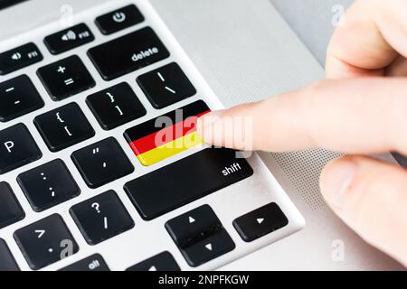 Online-Internationales Geschäftskonzept: Computerschlüssel mit deutscher Flagge darauf. Männliche Hand drückt Computerschlüssel mit deutscher Flagge Stockfoto