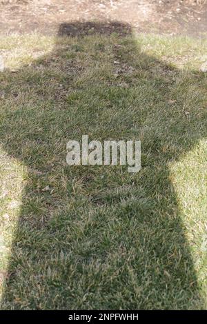 Der Schatten eines keltischen Kreuzes, das auf den Rasen fällt. Stockfoto