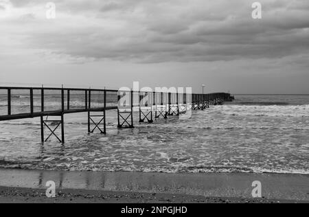 Minimale schwarz-weiße Landschaft mit langem Pier im Meer Stockfoto