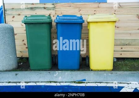 Grüne, blaue und gelbe Abfalleimer stehen hintereinander, Vorderansicht Stockfoto