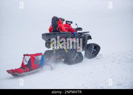 Das Bergrettungsteam ist unterwegs, um im Winter eine Person in den Bergen zu retten, mit einem Raupenfahrzeug und einem Schlitten Stockfoto