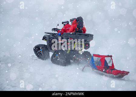 Das Bergrettungsteam ist unterwegs, um im Winter eine Person in den Bergen zu retten, mit einem Raupenfahrzeug und einem Schlitten Stockfoto