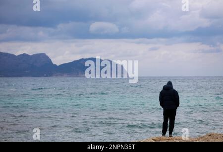 Santa Margalida, Spanien. 26. Februar 2023. Ein Mann schaut auf das Meer am Strand von Can Picafort. In den nächsten Tagen wird mit Regenwetter und sinkenden Temperaturen gerechnet. Kredit: Clara Margais/dpa/Alamy Live News Stockfoto