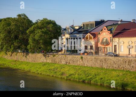 Stadtbild mit Fluss uzh. Ufer der Innenstadt mit alten Gebäuden am anderen Ufer in der Ferne. Sonniger Sommermorgen Stockfoto