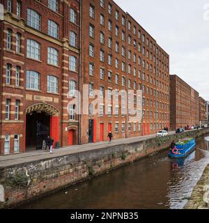 Ein blaues, schmales Boot stellt im Februar 2023 einen Kontrast zu den traditionellen roten Ziegeln der Royal Mill entlang der Redhill Street in der Ancoats Gegend von Manchester dar. Stockfoto