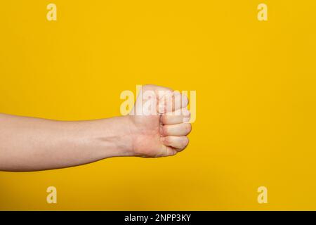 Die Hand eines starken Mannes in Form einer Faust waagerecht, isoliert auf gelbem Hintergrund. Die Faust ist bereit, zu schlagen und zu verletzen. Stockfoto