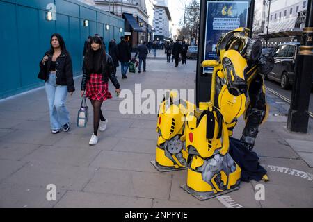 Passanten von On Oxford Street interagieren mit dem leeren Kostüm eines Straßenkünstlers, der sich am 6. Februar 2023 in London, Großbritannien, als gelber Transformer kleidet. Transformers ist ein Medienkonzern, das von der amerikanischen Spielzeugfirma Hasbro und dem japanischen Spielzeugkonzern Takara Tomy produziert wird. Es folgt hauptsächlich den heldenhaften Autobots und den bösen Decepticons. Stockfoto