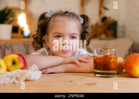 Süßes kleines Mädchen in der Küche zu Hause mit Äpfeln und einem Glas Apfelsaft. Umweltfreundliche Kinderkost. Platz für Text. Hochwertiges Foto Stockfoto