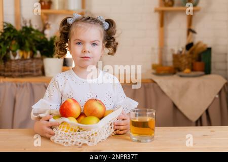 Süßes kleines Mädchen in der Küche zu Hause mit Äpfeln und einem Glas Apfelsaft. Umweltfreundliche Kinderkost. Platz für Text. Hochwertiges Foto Stockfoto