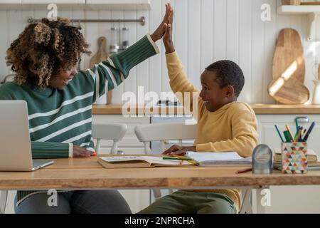 Ein glücklicher Schuljunge und Privatlehrer, der High Five am Heimtisch gibt, um den Studienerfolg zu feiern Stockfoto