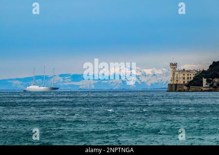 Triest, Italien, 26. Februar 2023- A 'Fata Morgana', eine komplexe Form überlegener Fata, sichtbar in einem schmalen Band direkt über dem Horizont, eine atmosphärische Refraktion, die sehr weit entfernte Dolomiten-Berge von der Küste von Triest aus sichtbar macht, hinter dem Miramare-Palast (R) und der größten Segel-gestützten Superyacht, die je gebaut wurde, Die 143m (470ft) "Segeljacht A" gehört dem russischen Oligarchen Andrej Igorevich Melnichenko, der von den italienischen Behörden im Rahmen der westlichen Sanktionen gegen Moskau wegen seines Krieges in der Ukraine beschlagnahmt wurde. Der Begriff Fata Morgana ist eine italienische Übersetzung von "Morgan, die Fee", der "d" war Stockfoto