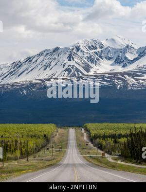 Der Alaska Highway fährt im Frühling in die Stadt Haines Junction mit epischen, riesigen Bergen in weiter Ferne und einer atemberaubenden Panoramastraße. Stockfoto