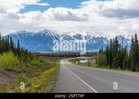 Der Alaska Highway fährt im Frühling in die Stadt Haines Junction mit epischen, riesigen Bergen in weiter Ferne und einer atemberaubenden Panoramastraße. Stockfoto