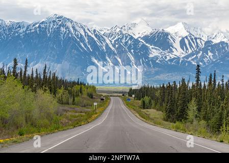 Der Alaska Highway fährt im Frühling in die Stadt Haines Junction mit epischen, riesigen Bergen in weiter Ferne und einer atemberaubenden Panoramastraße. Stockfoto