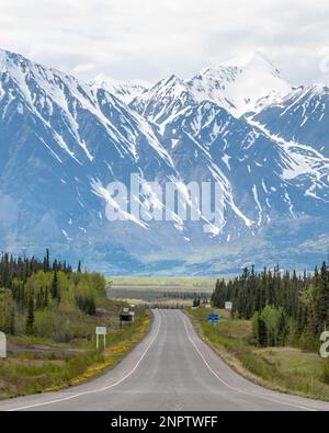 Der Alaska Highway fährt im Frühling in die Stadt Haines Junction mit epischen, riesigen Bergen in weiter Ferne und einer atemberaubenden Panoramastraße. Stockfoto