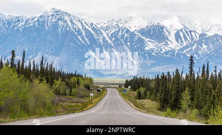 Der Alaska Highway fährt im Frühling in die Stadt Haines Junction mit epischen, riesigen Bergen in weiter Ferne und einer atemberaubenden Panoramastraße. Stockfoto