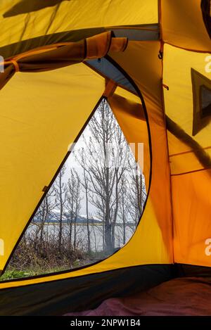 Vor einem gelben Zelt, während Sie im Norden Kanadas campen, mit trockenen Bäumen im Frühling, die auf den Sommer warten, am bewölkten Nachmittag. Stockfoto