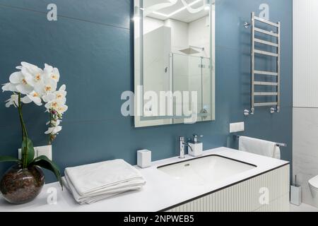 Badezimmer in Blau und Weiß mit großem Spiegel, Handtüchern, Beleuchtung und Waschbecken. Sauberes und frisches Bad mit modernem Licht. Geräumiges Badezimmer, sauber, Stockfoto