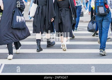 Fußgänger überqueren den Fußgängerübergang. Junge Leute in schwarzen Kleidern, stilvolle Hipster-Mädchen, die durch die Stadt laufen Stockfoto