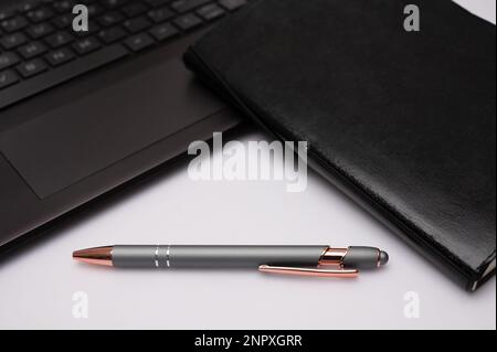 Ein schwarzes Notizbuch mit einem Stift und einem Computer auf einem Desktop, das ein Gefühl für ein Heimbüro oder kreatives Schreiben vermittelt. Stockfoto