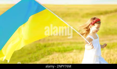 Die blau-gelbe Flagge der Ukraine, die am Tag der Unabhängigkeit der Ukraine in den Händen eines kleinen ukrainischen Mädchens im Wind weht. Symbole der Ukraine in den Händen eines Lächelns Stockfoto