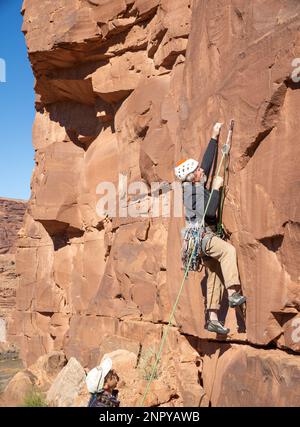 Männlicher Erwachsener steilt ein steiles Felsgesicht hinauf. Moab, Utah Stockfoto