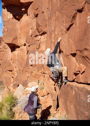 Männlicher Erwachsener steilt ein steiles Felsgesicht hinauf. Moab, Utah Stockfoto