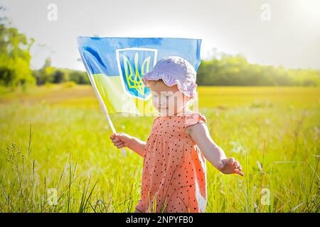 Die blau-gelbe Flagge der Ukraine, die am Tag der Unabhängigkeit der Ukraine in den Händen eines kleinen ukrainischen Mädchens im Wind weht. Symbole der Ukraine in den Händen eines Lächelns Stockfoto