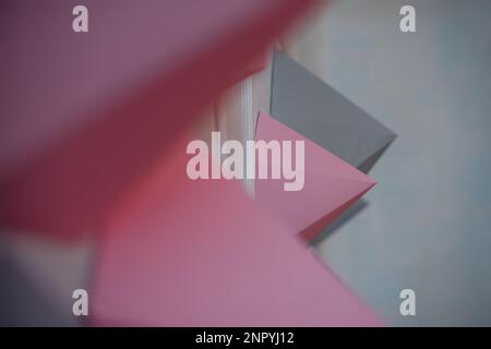 Abstrakter Hintergrund von Papierpolygonen in Grau, Pink, verschiedenen Formen auf einer weißen Wand. Kreative Inneneinrichtung. Dynamische Figuren im Innenraum. Origami h Stockfoto