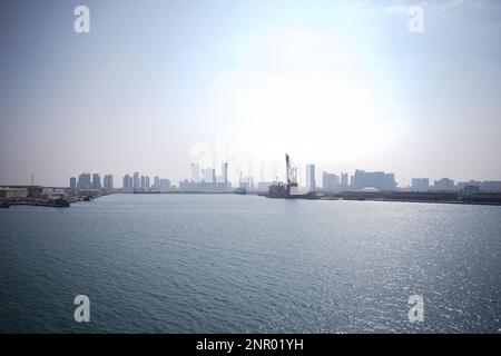 Ein riesiges Gebäude, viele Turmbaustellen mit Kränen und Gebäuden vor dem Meer. Blick von der Bootstour. Abo Dhabi, Vereinigte Arabische Emirate Stockfoto